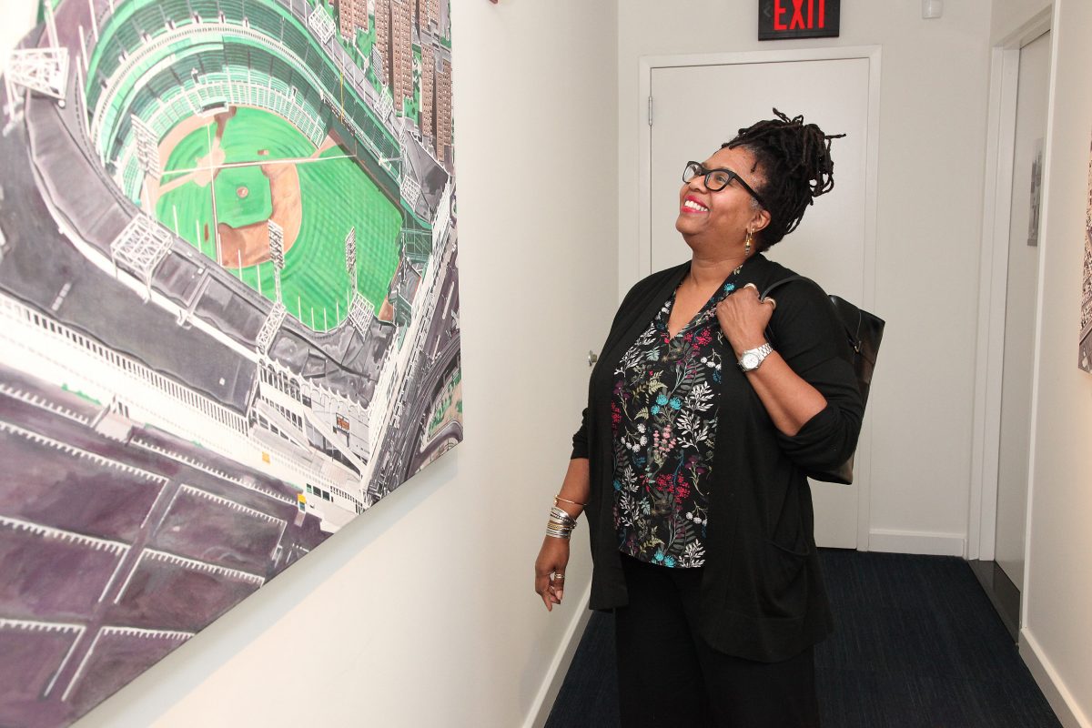 Pat Moore, wide of artist Andy Jurinko, standing in front of one of Jurinko's stadium paintings