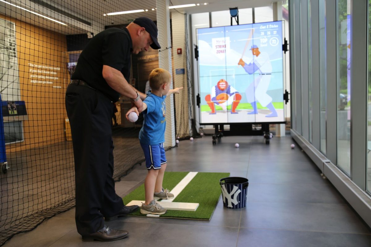 Young boy about to pitch a baseball, with help from an adult man, at the Pitch! exhibition