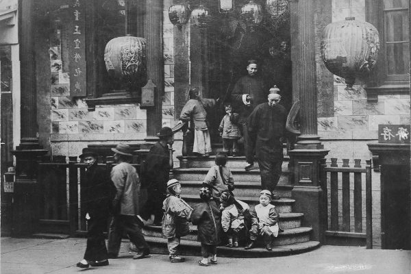 Black and white photo of a group of Chinese immigrants on a staircase with Chinese lanterns in the doorway.