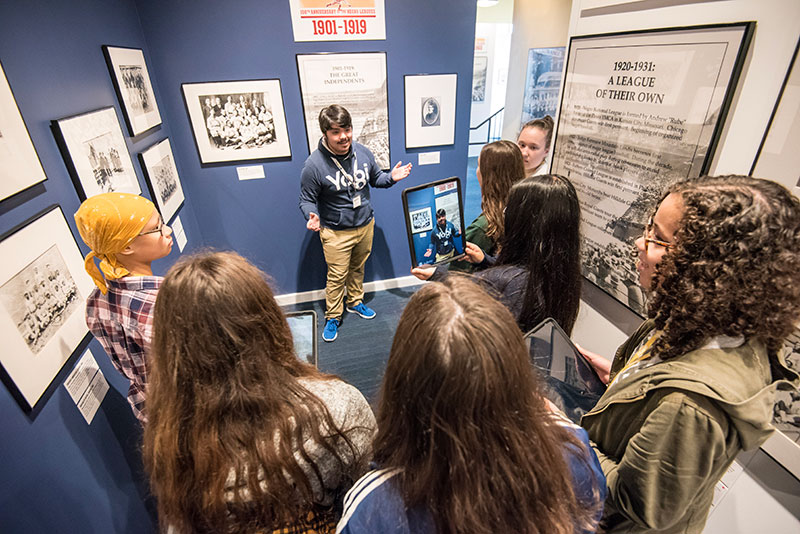 A Museum guide with a group of students at the Discover Greatness exhibition