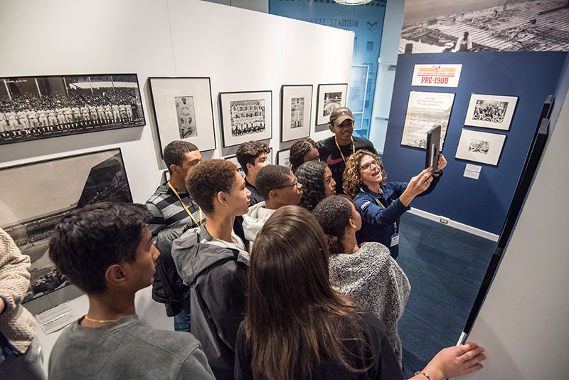 A Museum guide showing a group of students the augmented reality feature of the Discover Greatness exhibition