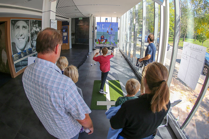 Boy throwing a baseball, surrounded by family as part of the Pitch! exhibition