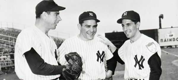 Black & white photo of Joe DiMaggio, Yogi Berra and Phil Rizzuto standing together on a baseball field