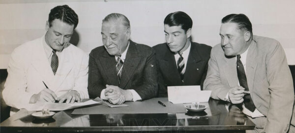 Three men in suits overlooking Lou Gehrig signing a contract