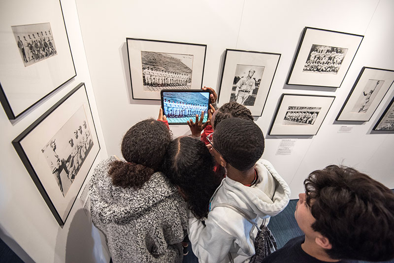 Students hold up an iPad with a colorized photo from the exhibit.