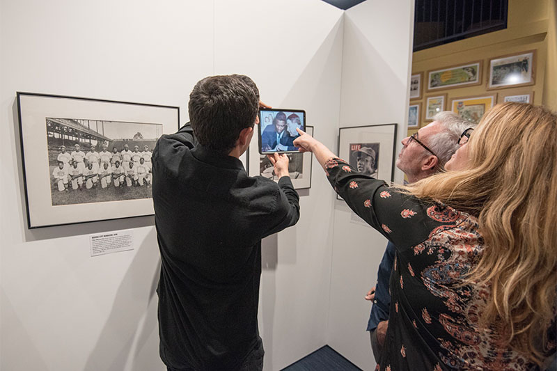 Viewers hold up and point at an iPad with colorized photos from the exhibit.